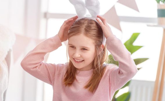 Cute little girl wearing bunny ears looking back and smiling at Easter day