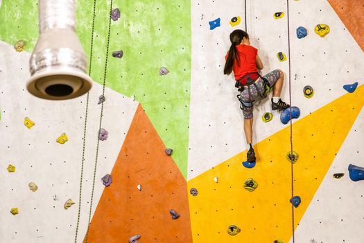 Sporty little girl climbing artificial boulder on practical wall in gym