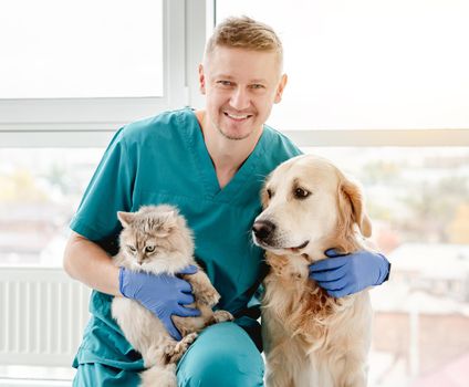 Happy veterinarian hugging golden retriever dog and fluffy cat in clinic