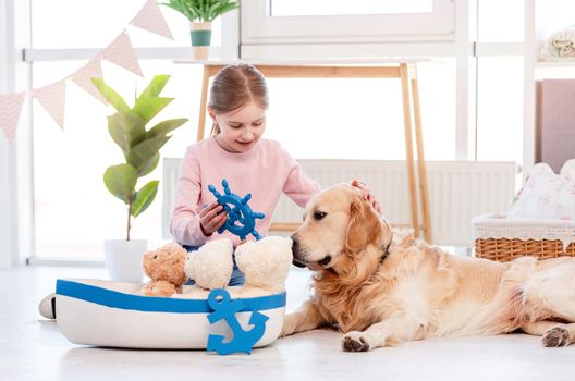Little girl playing role marine games with golden retriever dog. Sea ship toy and child