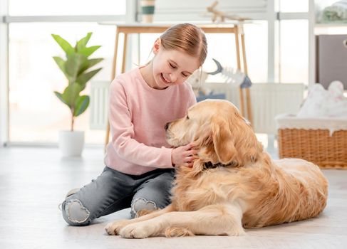 Little cute girl sitting with smile on her face on the floor and petting golden retriever dog