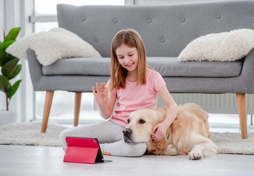 Beautiful girl sitting on the floor with golden retriever dog and talking with family friends online on tablet