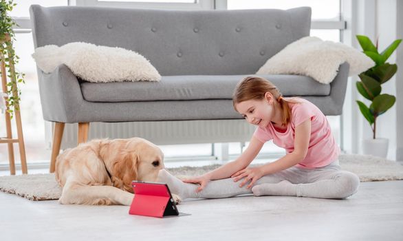 Girl sitting on the floor with golden retriever dog and exercising online with tablet