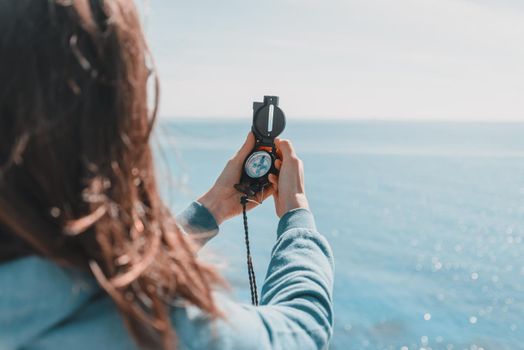 Traveler woman searching direction with a compass on coastline near the sea in summer