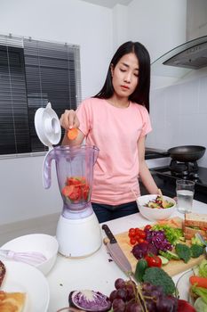 young woman making smoothies with blender in kitchen