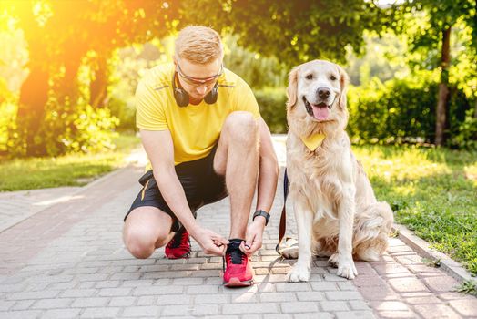 Golden retriever sitting near sportsman tying shoelace while running in park