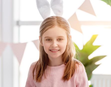 Portrait of little beautiful girl wearing bunny ears and staying in the room full of sunlight