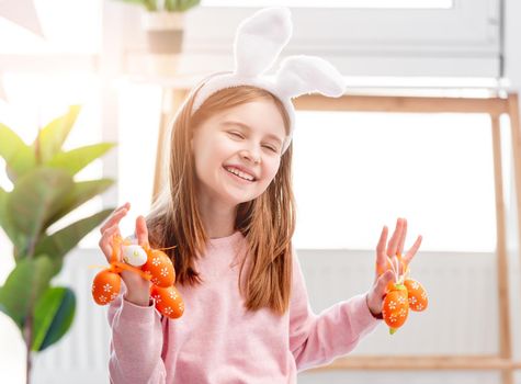 Beautiful little girl holding painted eggs in her hands and smiling at Easter day. Cute child wearing bunny ears
