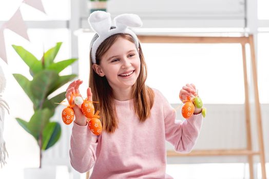 Beautiful little girl wearing bunny ears holding painted eggs in her hands and smiling at Easter