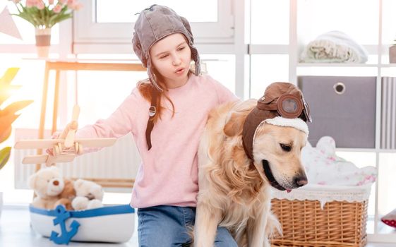 Little girl playing role games as plane pilot with golden retriever dog