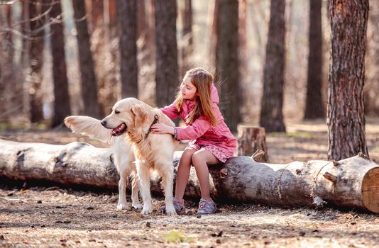 Beautiful preteen girl sitting on log with golden retriever dog in the wood