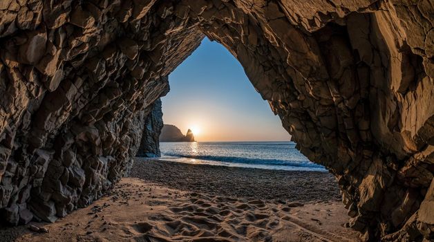 view from the stone cave on the sunset, sea and the beach, the volcanic rock of the cave is lit by the warm setting sun. volcanic basalt as in Iceland Beauty world, nature and outdoors travel concept