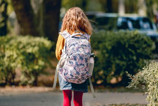Preteen school girl with backpack outdoors from back. Pretty pupil female kid wit bag after education class in autumn park