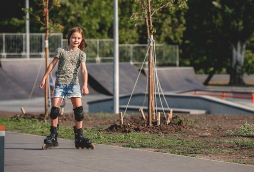 Pretty girl child on roller skates riding in city. Beautiful female preteen kid rollerblading at summer