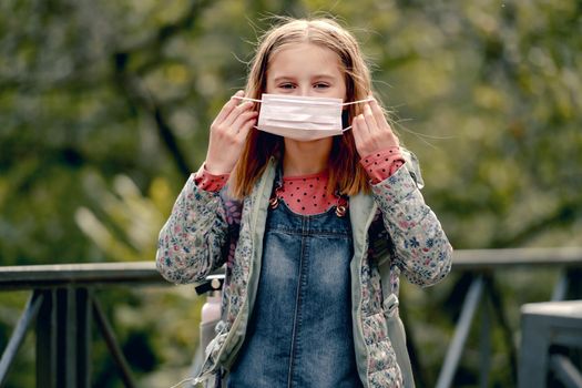 Pretty school girl wearing face mask and looking at camera. Beautiful female kid after school in pandemic coronavirus time