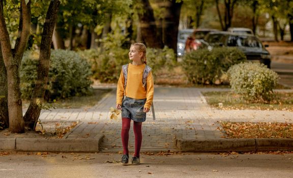 Preteen school girl with backpack holding yellow leaves in her hand and walking. Pretty pupil female kid after education class in autumn park