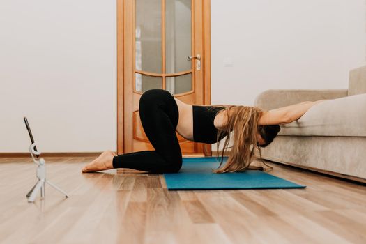 Young woman with long hair, fitness instructor in black sportswear, doing stretching and pilates on yoga mat at home. Female fitness yoga routine concept. Healthy lifestyle harmony and meditation