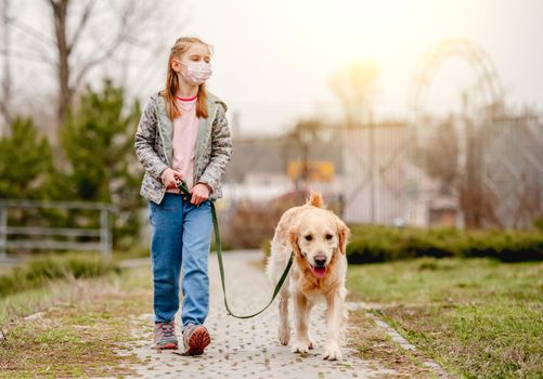 Cute preteen girl wearing mask walking with golden retriever dog in coronavirus time