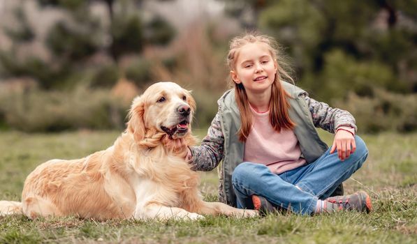 Little beautiful girl sitting on the grass with golden retriever dog outside