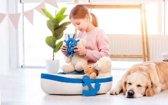 Little girl looking at steering wheel toy and golden retriever dog sleeping close to her