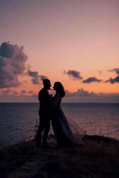 silhouettes of a happy young couple guy and girl on a background of orange sunset in the ocean