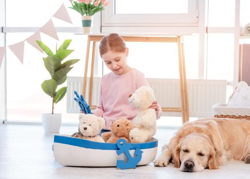 Little girl playing with marine toys on the floor and sitting close to sleeping golden retriever dog