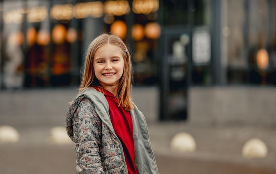 Preteen girl in autumn day looking at camera and smiling. Pretty kid portrait outdoors with blurred background