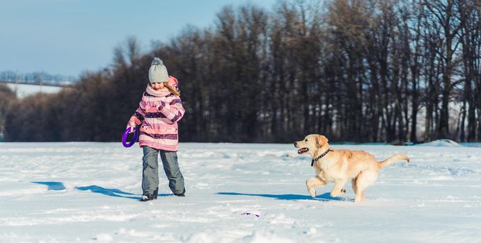 Happy little girl playing with cute dog outside on snowy field