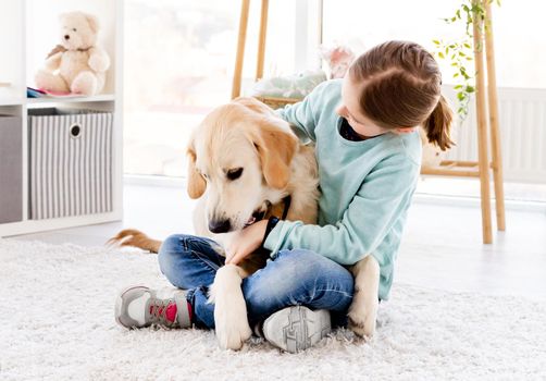 Pretty little girl holding cute dog sitting on floor indoors