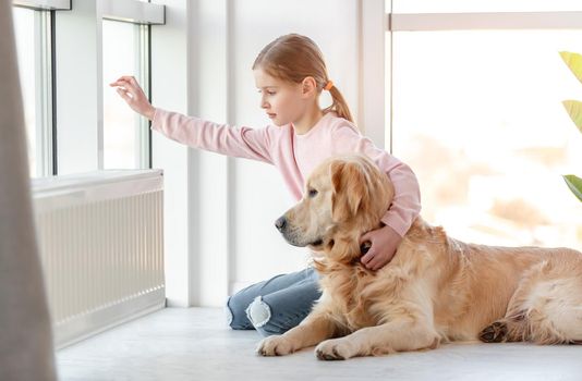 Little girl child with golden retriever dog sitting on the floor and looking out the window