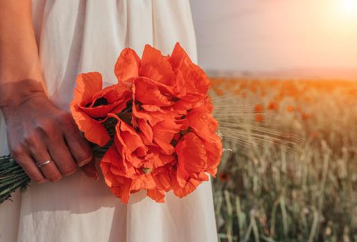 Bride in a white dress holding a bouquet of poppy flowers, warm sunset time on the background of the lavender field. Copy space. The concept of calmness, silence and unity with nature.