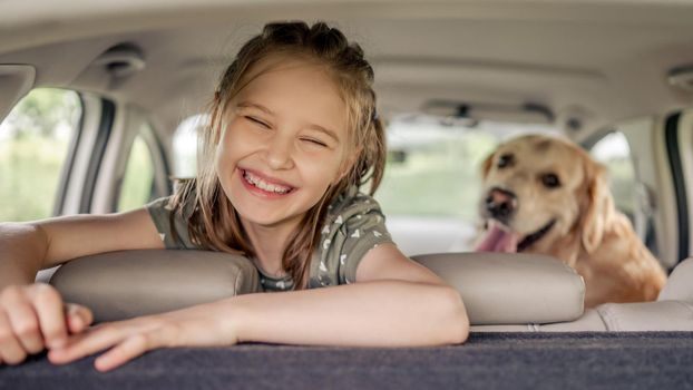 Preteen girl with golden retriever dog sitting in the car, looking at the camera and smiling. Child kid with purebred doggy pet in the vehicle inside