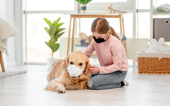 Little girl and golden retriever dog wearing masks at home in pandemic time