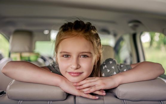 Cute preteen girl with hairstyle sitting in the car, looking at the camera and smiling. Child kid in the vehicle inside during summer trip