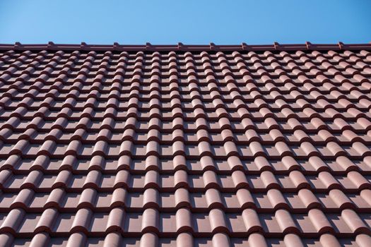 Brown tile roof under blue sky. The photo is divided on two part. One part is a roof made of clay tiles and the other is a pure blue sky background. Place for text