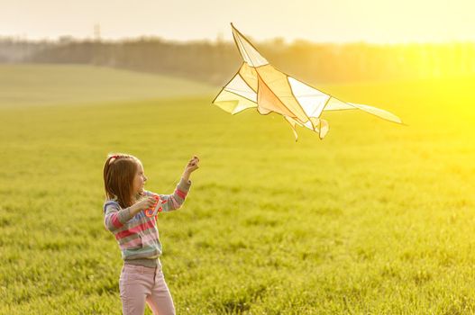 Beautiful little girl with flying kite on sunny field