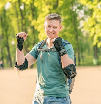 Handsome man wearing protection for active sport in green tshirt smiling, standing in the park