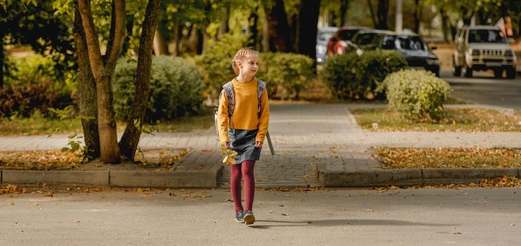 Preteen school girl with backpack holding yellow leaves in her hand and walking. Pretty pupil female kid after education class in autumn park