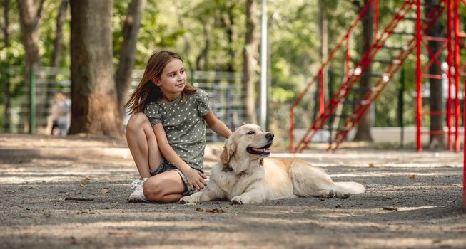 Preteen girl with golden retriever dog sitting on the earth in the park. Cute child with doggy pet portrait outdoors