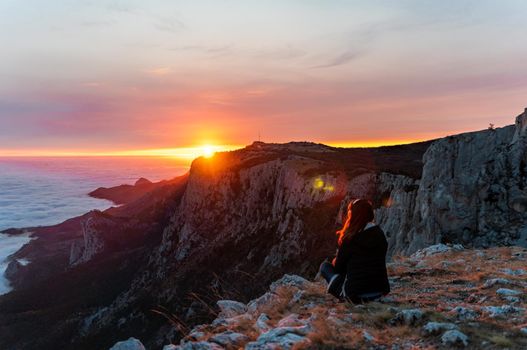 Beautiful tourist woman sitting on a rock high in the mountains, above the clouds and enjoying the sunset Copy space. The concept of calmness, silence and unity with nature.