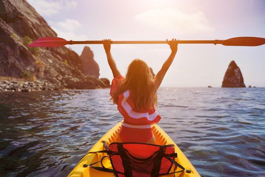 Young brunette woman in red swimsuit and Santa hat, swimming on kayak around basalt rocks like in Iceland. Back view. Christmas and travel concept