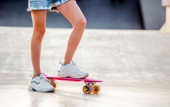 Legs of girl standing on skateboard outdoors. Female skater child riding on skate in the city