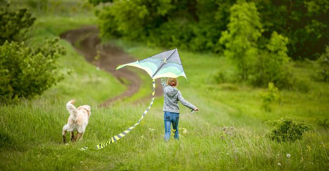 Back view of little girl with cute dog flying colorful kite on spring nature