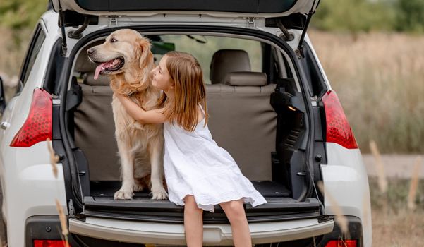 Pretty girl hugging golden retriever dog in car trunk and looking back together. Cute little child kid with doggy pet in vehicle at nature