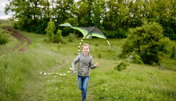 Happy little girl flying bright kite outdoors on nature in spring