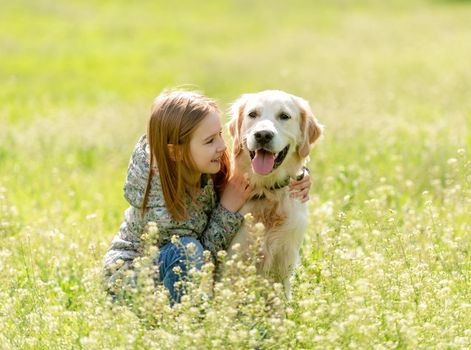 Smiling little girl looking at cute dog sitting in flowers on sunny field