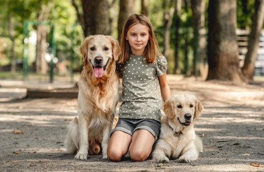 Cute girl child with two golden retriever dogs outdoors. Preteen female kid with pets in the park