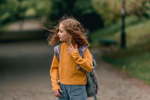 Beautiful girl child with back pack after school looking back at the street at autumn. Portrait of preteen female kid outdoors