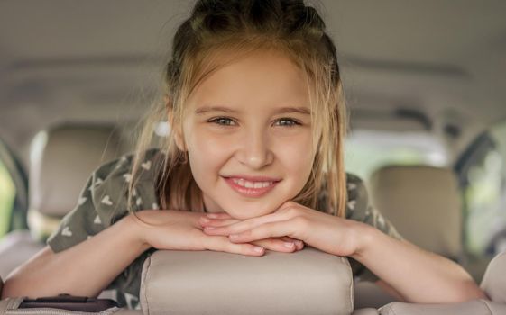 Cute preteen girl with hairstyle sitting in the car, looking at the camera and smiling. Child kid in the vehicle inside during summer trip