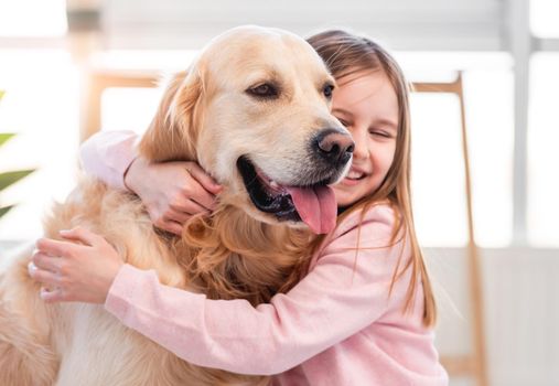 Pretty little girl hugging golden retriever dog and smiling. Portrait of friendship